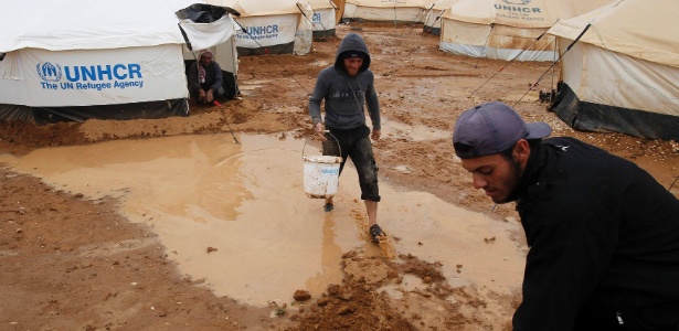 Refugiados sírios tentam limpar a sujeira provocada pelas fortes chuvas que atingiram a região do acampamento da ONU para abrigar a população síria, na fronteira da Síria com a Jordânia