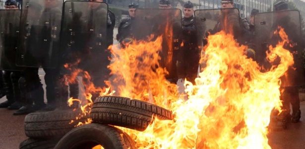 Policiais franceses se abrigam atrás de pneus incendiados durante manifestação contra o corte de empregos na Goodyear, nos arredores de Paris. A empresa confirmou em janeiro o fechamento da fábrica, acabando com 1.173 postos de trabalho na região