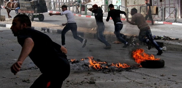 Palestinos correm pela região central de Hebron, na Cisjordânia, durante confronto da polícia fronteiriça de Israel com manifestantes contrários à expansão de assentamentos judaicos 