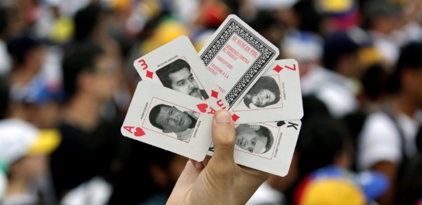 Carlos Garcia Rawlins/ Reuters Manifestante mostra cartas de baralho com as imagens de Hugo Chávez e Nicolás Maduro durante protesto de opositores ao governo venezuelano, em Caracas