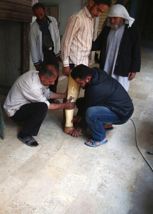 Homem experimenta perna protética enquanto outro aguarda em uma "oficina do bem-estar" no bairro Duma, em Damasco, na Síria