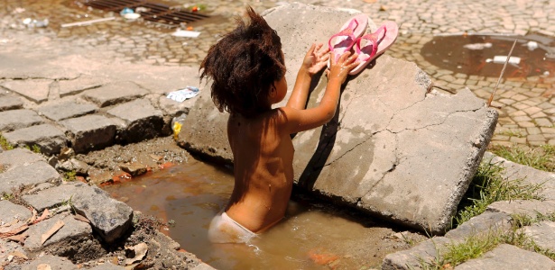 Criança toma banho em bueiro cheio de água suja no centro do Rio de Janeiro