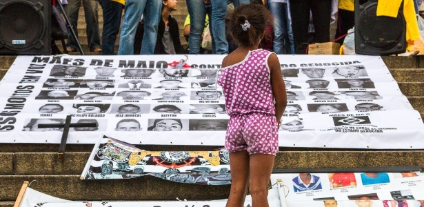 Criança observa cartaz com fotos de jovens vítimas de violência na periferia de São Paulo