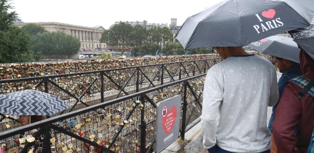 Turistas observam placa que diz "nossas pontes não resistirão ao seu amor", na Pont Neuf, em Paris