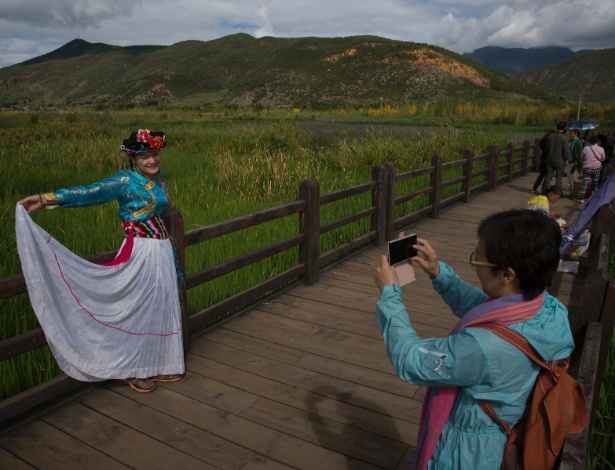 Turista chinesa de Hong kong tira foto com traje típico da etnia Mosou, em ponte sobre o lago Lugu, em Luoshui, na China