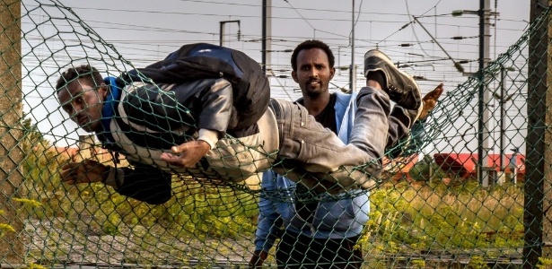 Imigrantes pulam a cerca em Coquelles, próximo a Calais, no norte da França, para chegar à ferrovia que leva ao terminal do Eurotúnel