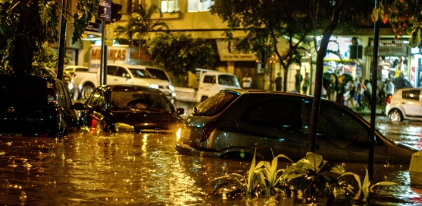 Carros ficam parcialmente encobertos em rua inundada durante chuva forte no Rio de Janeiro