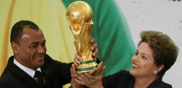 Dilma Rousseff, ao lado do o ex-jogador e campeão do mundo Cafu, levanta a taça da Copa após recebê-la do presidente da Fifa, Joseph Blatter, durante cerimônia no Palácio do Planalto na semana passada